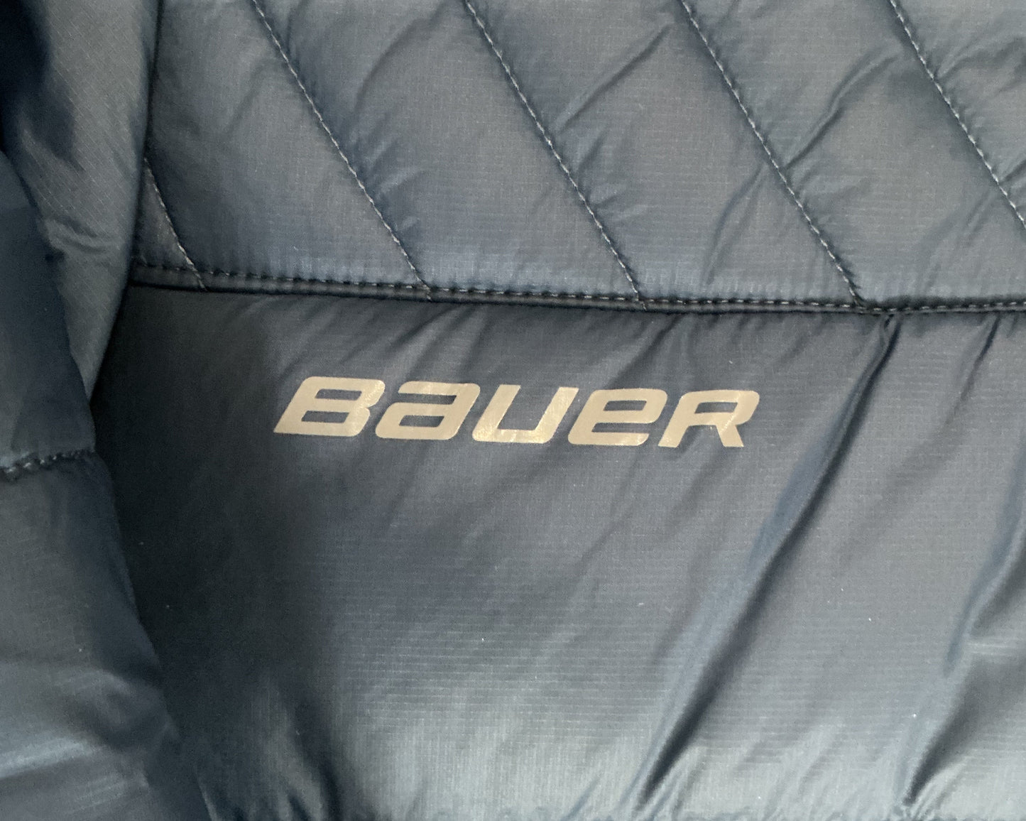 Gray quilted jacket with 'Bauer' branding on a close-up view